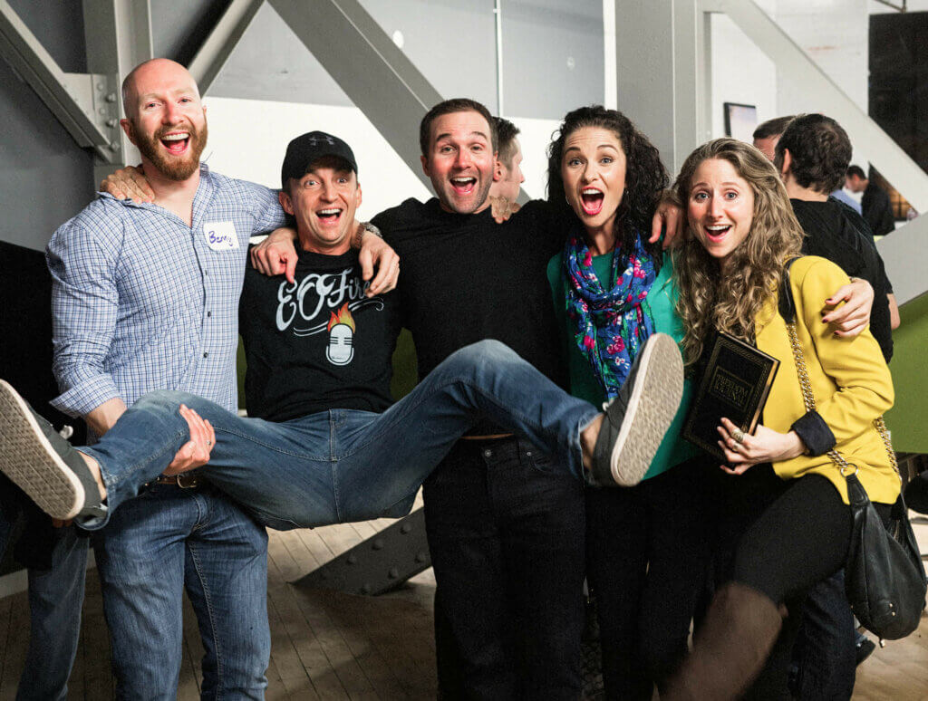Picture of John, Kate, and three other people in an event space. They all look very happy and one guy is being lifted off of the ground.