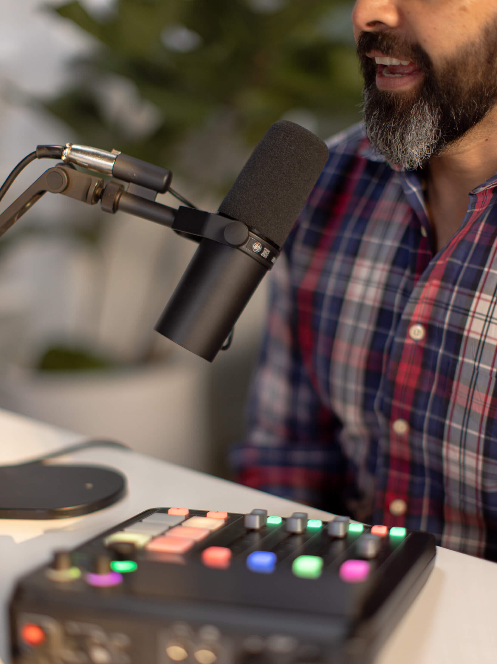 Talking into a podcast microphone with a control board on the desk