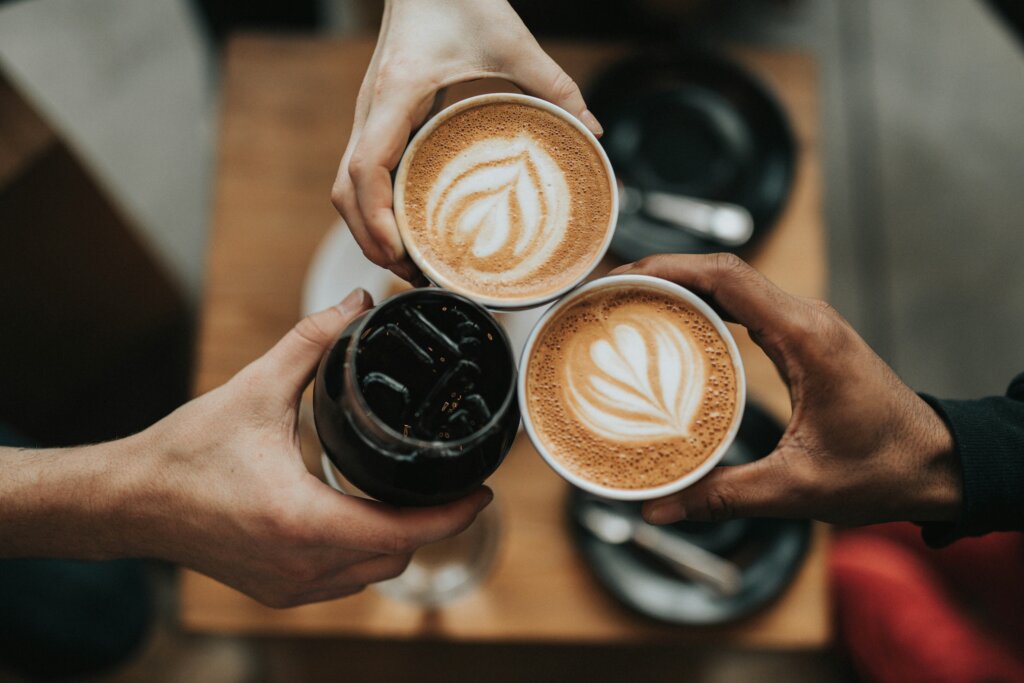 Three hands toast coffee drinks, shot from above.